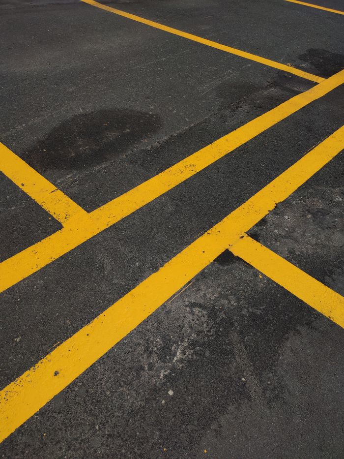 services-img Close-up of bright yellow lines marking a parking area on dark asphalt pavement.