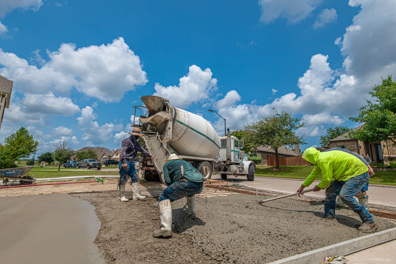 about-img Construction workers laying concrete for a driveway in Fort Worth, Texas, under a bright blue sky.