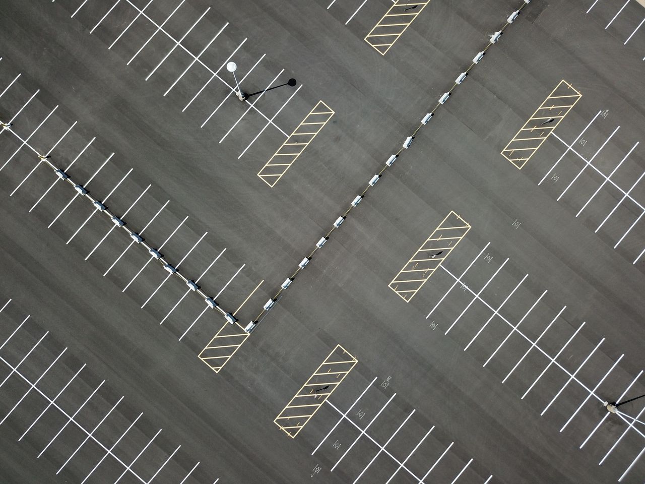 contact-img Top-down view of a large, empty parking lot featuring clear lines and patterns.